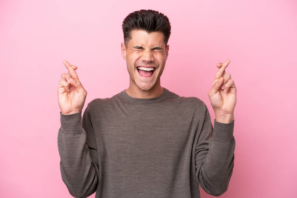 Young caucasian man isolated on pink background with fingers crossing - Photo, Image
