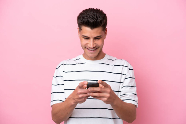Jovem caucasiano isolado em fundo rosa enviando uma mensagem com o celular - Foto, Imagem