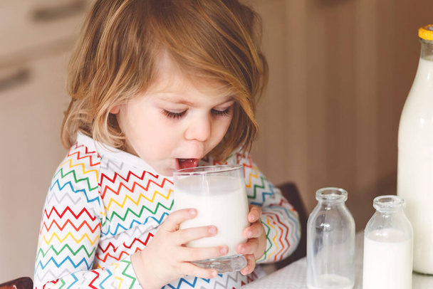Suloinen pikkutyttö juo lehmänmaitoa aamiaiseksi. Söpö tytär, jolla on paljon pulloja. Terveellinen lapsi, jolla on maitoa terveyskalsiumin lähteenä. Lapsi kotona tai lastentarhassa aamulla - Valokuva, kuva