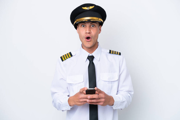 Vliegtuig Kaukasische piloot geïsoleerd op witte achtergrond verrast en het verzenden van een bericht - Foto, afbeelding