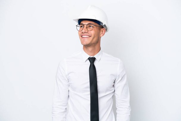 Young architect caucasian man with helmet and holding blueprints isolated on white background thinking an idea while looking up - Photo, image