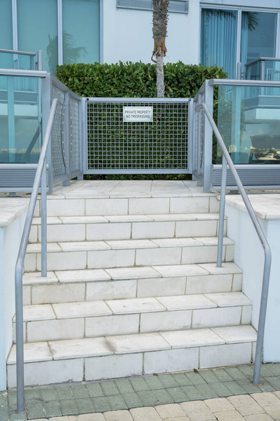 Entrada de escada com propriedade privada Sem sinal de invasão em um portão railings- Miami, Florida. Escadas com azulejos e corrimãos que levam a um pequeno portão perto do arbusto e do edifício ao fundo. - Foto, Imagem