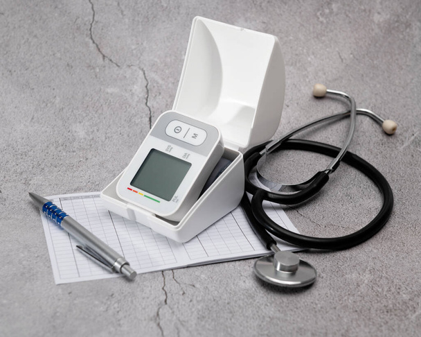 Automatic digital wrist blood pressure monitor; pressure monitoring chart; pen; stethoscope; on gray background - Photo, Image