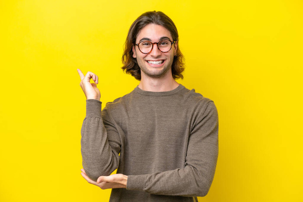 Caucasian handsome man isolated on yellow background happy and pointing up - Photo, Image