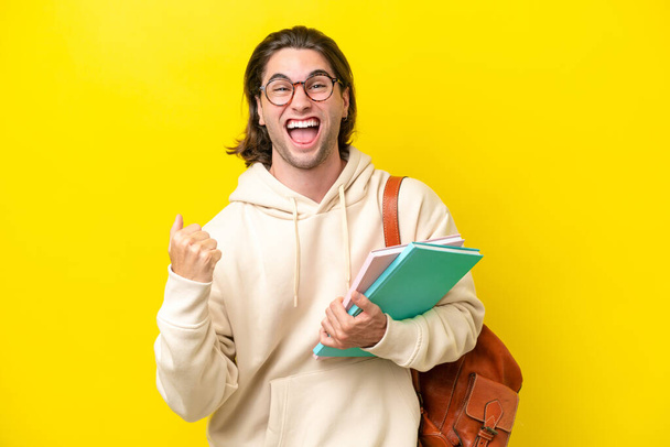 Young student handsome man isolated on yellow background celebrating a victory in winner position - Photo, image