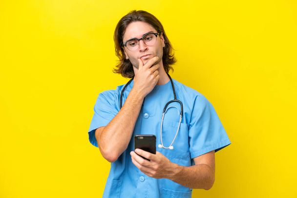 Young surgeon caucasian man isolated on yellow background thinking and sending a message - Fotoğraf, Görsel
