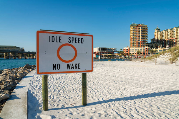 Idle Speed No Wake znamení na bílém písku na pobřeží pláže v blízkosti hotelů v Destin, Florida. Rozcestník u vody a mostu vlevo a hotelové budovy vpravo. - Fotografie, Obrázek