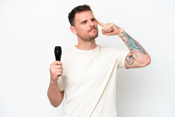 Mladý běloch zpěvák muž zvedání mikrofon izolované na bílém pozadí s pochybnostmi a myšlení - Fotografie, Obrázek