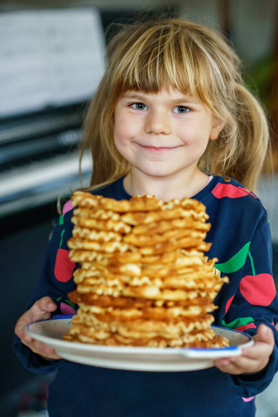 Portré egy boldog óvodás lányról, aki friss palacsintát tart. Mosolygó éhes kisgyerek édes keksz ostyával. Édes cukor belgiai gofri - Fotó, kép