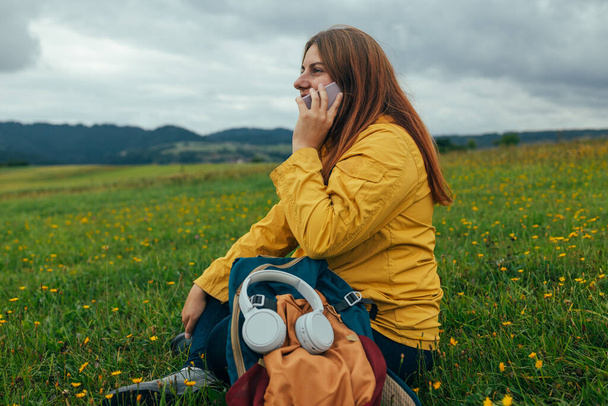 Shot of a young woman enjoying a day in nature sitting in mountain field and using phone call in nature - Φωτογραφία, εικόνα