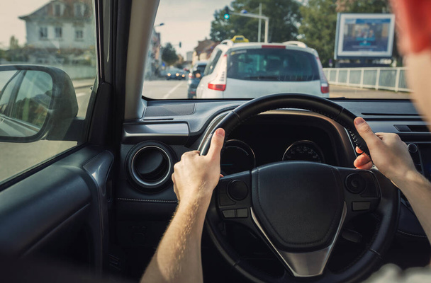 Mężczyzna prowadzący samochód na ulicy miejskiej, zbliżenie rąk na kierownicy - Zdjęcie, obraz