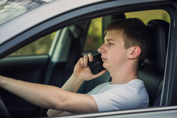Young man unsafe driving while phone talking in front of the steering wheel. Careless driver violates traffic rules - Foto, Imagem