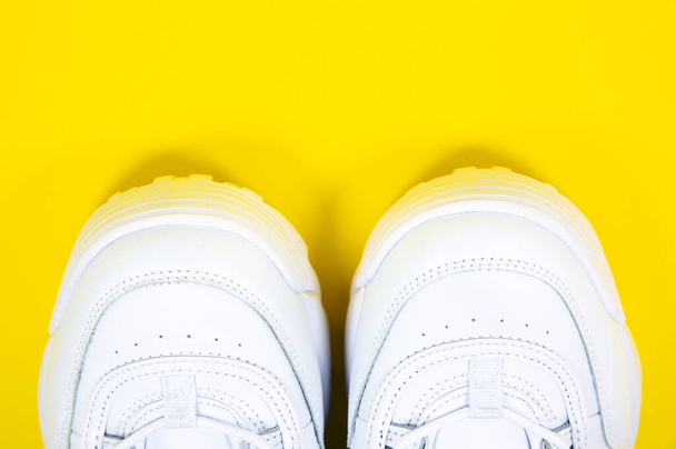 Μοντέρνα αθλητικά παπούτσια στο κίτρινο φόντο. Άσπρα δερμάτινα αθλητικά παπούτσια σε μεγάλη σόλα με καρφιά. Κλείσε.. - Φωτογραφία, εικόνα