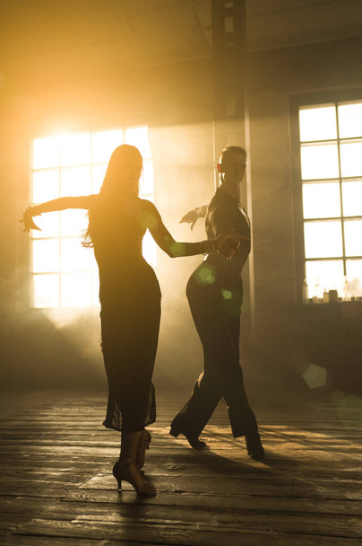 Δυο επαγγελματίες χορευτές χορεύουν στο στούντιο της σοφίτας. Όμορφη καλλιτεχνική παράσταση με βαρύ καπνό. Αθλητική ζωή έννοια. Πάθος και συναισθηματικός χορός. - Φωτογραφία, εικόνα
