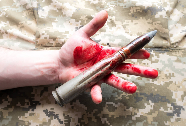 Shell missiles with blood in mans hand on khaki jacket background. No war, army concept. - Photo, image