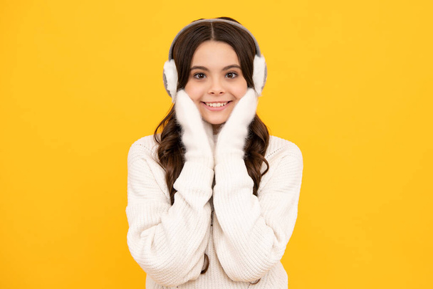 Teenager girl with winter warm earmuff ear-flaps hat over isolated yellow background. Winter christmas holidays, new year mood. Kids warm clothes - Foto, afbeelding