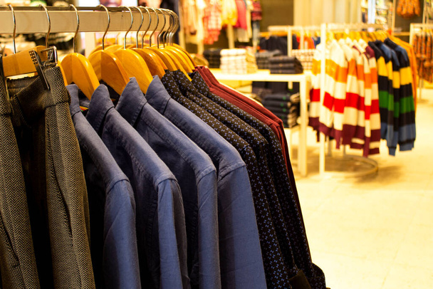 Shirt and pant hanging on hangers on a clothing rack and arranged in shelf in a modern clothe store - Photo, Image
