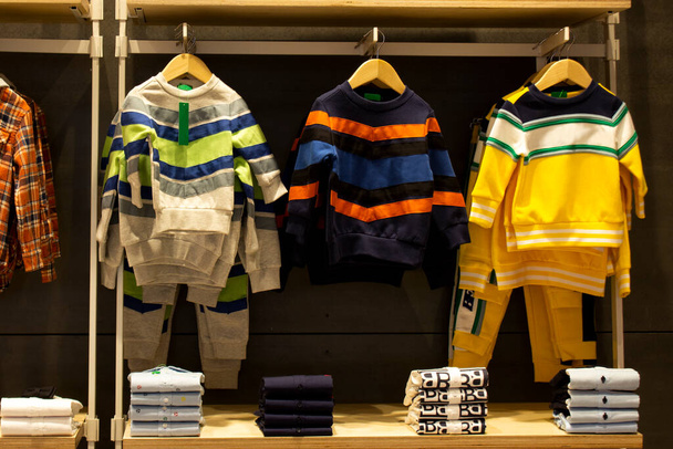 Koszula i spodnie wiszące na wieszakach na wieszaku na ubrania i ułożone na półce w nowoczesnym sklepie odzieżowym - Zdjęcie, obraz