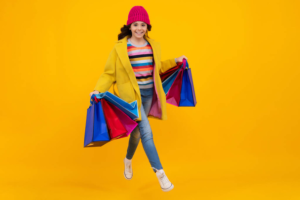 Funny teen girl hold shopping bag enjoying sale isolated on yellow. Portrait of teenager schoolgirl is ready to go shopping. Autumn shopping sale - Zdjęcie, obraz