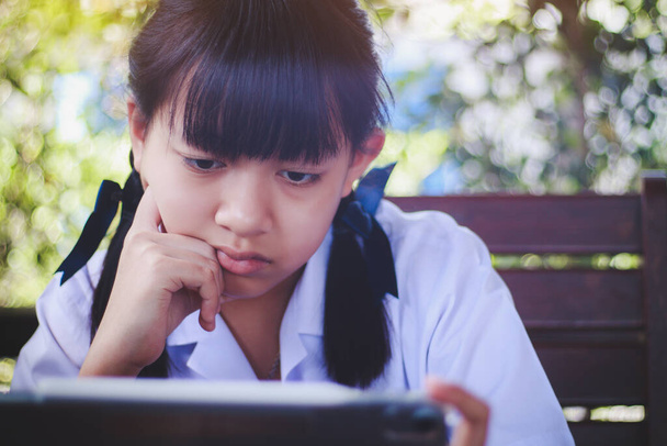 Ασιάτισσα νεαρή φοιτήτρια που κοιτάζει μια οθόνη tablet με μια στοχαστική και ανήσυχη έκφραση.Έννοια για τα εφηβικά προβλήματα και τη χρήση της τεχνολογίας επικοινωνίας - Φωτογραφία, εικόνα