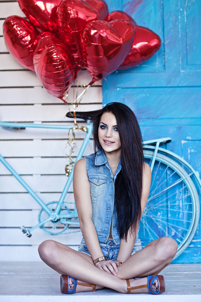 Beautiful brunette young woman in jeans  with a heart-shaped balloons near bicycle. Valentine's day. - Foto, afbeelding