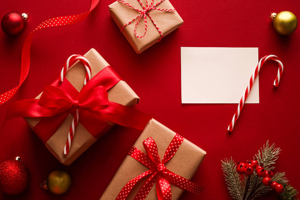 Weihnachtsschmuck, Geschenke und Dekoration mit weißem leeren Gruß oder Visitenkarte oder Danksagung auf festlichem rotem Hintergrund als frohe Feiertage flach. - Foto, Bild