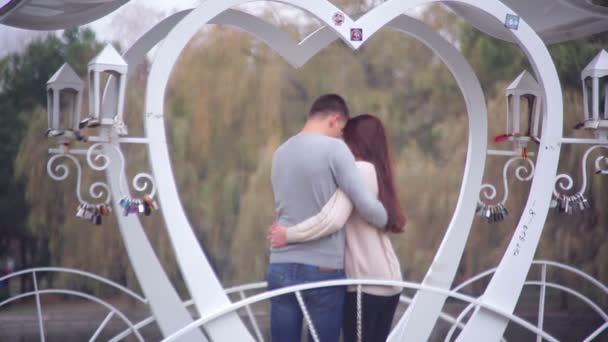 Miłości para stojący w altanie w formie serca w parku - Materiał filmowy, wideo