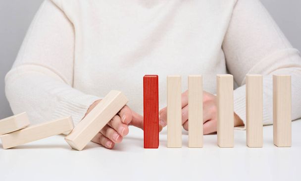 Hand stops the fall of wooden blocks on a white background. Concept of a strong and courageous personality capable of withstanding unequal difficulties. Strong business, control of the situation - Photo, Image