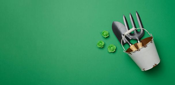 Miniaturowe narzędzia ogrodowe w metalowym wiadrze na zielonym tle, widok z góry - Zdjęcie, obraz