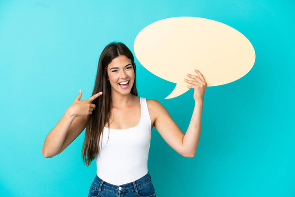 Young Brazilian woman isolated on blue background holding an empty speech bubble and pointing it - Foto, Imagen