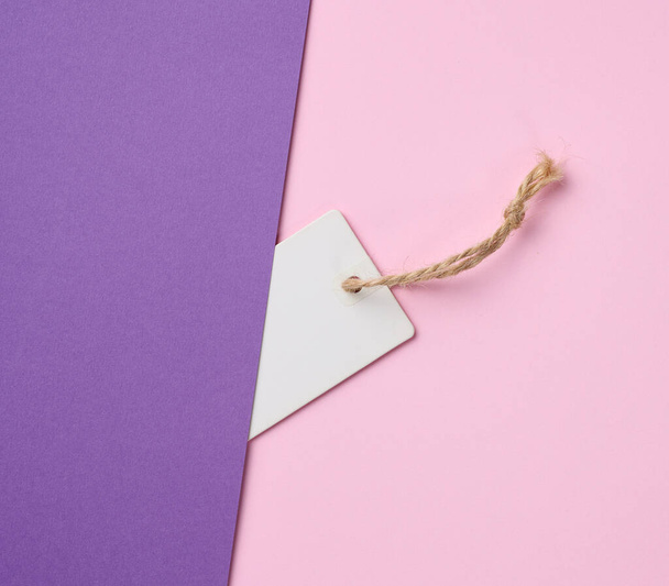 Étiquette vide en papier blanc sur une corde, fond rose. Modèle de prix, vue du dessus - Photo, image