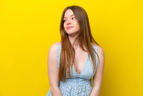 Young caucasian woman isolated on yellow background making doubts gesture looking side - Фото, зображення