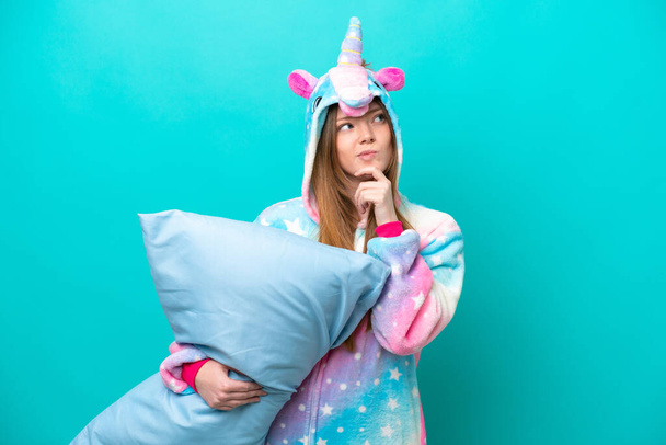Young caucasian girl with unicorn pajamas holding pillow isolated on blue background having doubts and thinking - Fotografie, Obrázek