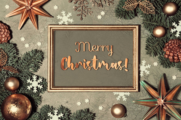 Christmas background. Flat lay with fir twigs decorated with red rowan berry, paper stars and snowflakes on grey green textured background. Greeting text Merry Christmas in frame. - Photo, Image