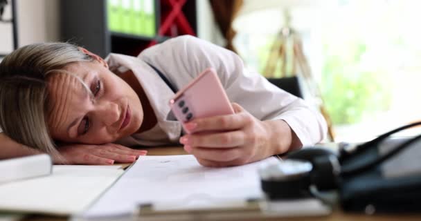 Fáradt unatkozó doktornő fekszik az asztalon mobiltelefonnal 4k film lassított felvétel. Nehézségek az orvostudomány koncepciójában - Felvétel, videó