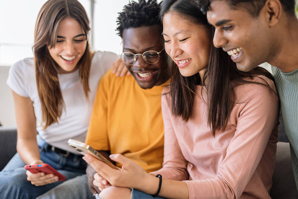 Junge multiethnische Gruppe von Teenagerfreunden, die zu Hause gemeinsam Mobiltelefone benutzen. Diverse Millennial-Studenten haben Spaß dabei, lustige Medieninhalte per Smartphone-App anzuschauen. Technologie-Lifestyle-Konzept - Foto, Bild