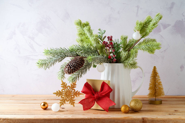 Christmas decoration with pine tree branches in vase, gift box  and golden ornaments on wooden table over bright background - Photo, Image