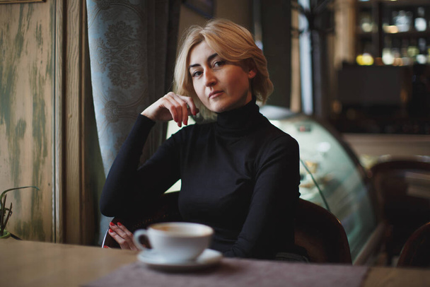 A beautiful woman is drinking coffee in a coffee shop - Fotoğraf, Görsel