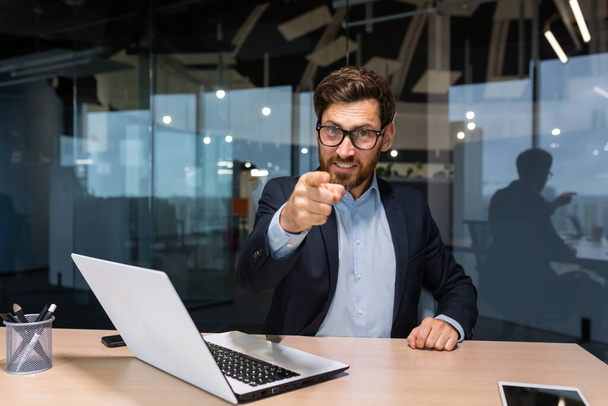 Successful mature businessman looking at camera and pointing finger forward calling to action, investor in business suit inside modern office working on laptop, boss with beard and glasses. - Foto, Imagen