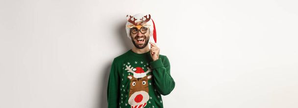 Vánoční a sváteční koncept. Usmívající se vousatý muž v klobouku Santa vypadá šťastně, drží party masku na Nový rok, slaví Vánoce, stojí nad bílým pozadím. - Fotografie, Obrázek