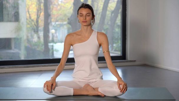 Beyaz elbiseli genç bayan yoga ve meditasyon egzersizleri yapıyor. Gittikçe daha fazla insan evinde ya da spor yaparak kendini kişisel refahına adıyor.  - Fotoğraf, Görsel