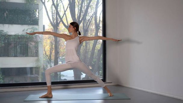 молода леді дівчина в білій сукні виконує вправи з йоги і медитації - все більше людей присвячують себе особистому благополуччю вдома або в спортзалі, займаючись спортом - способом життя вдома
  - Фото, зображення