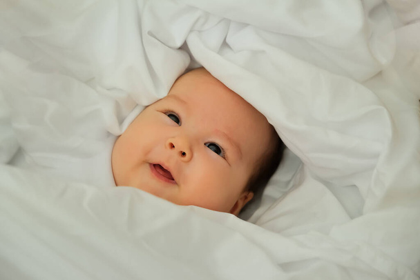 bebê recém-nascido sorri e ri. mostra emoções. bebê encontra-se em um pano branco - Foto, Imagem