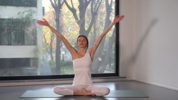 fiatal hölgy lány végez jóga meditációs gyakorlatok az ablak közelében - egyre több ember szenteli magát a személyes jólét otthon vagy a tornateremben sporttevékenységgel - életmód otthon - Felvétel, videó