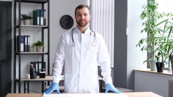 Retrato de un médico guapo en una clínica americana moderna. Un joven médico interno está mirando a la cámara y sonriendo. - Metraje, vídeo