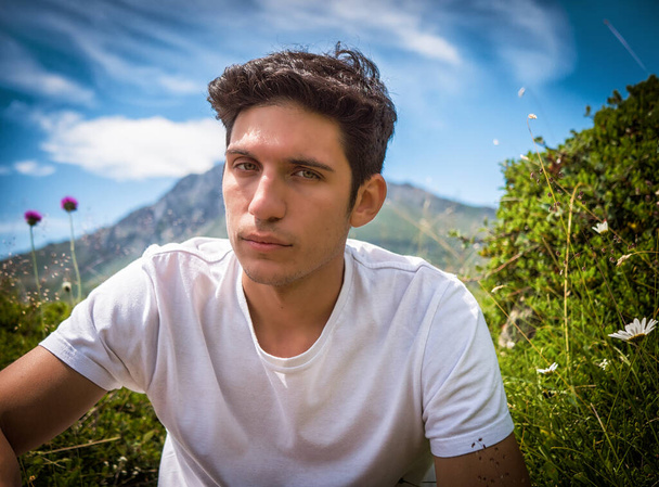 Handsome young man hiking in lush green mountain scenery looking at camera - Фото, изображение