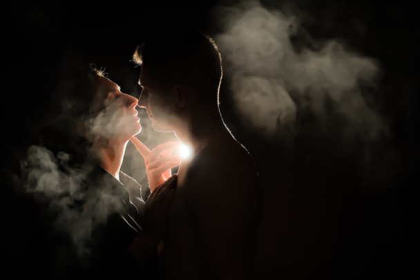 Η σιλουέτα ενός άντρα και μιας κοπέλας. Άντρες και γυναίκες στο σκοτάδι. καπνός. ατμός. Ένας άντρας και ένα κορίτσι σε ένα σκοτεινό δωμάτιο αγκαλιάζονται. έννοια της αγάπης. - Φωτογραφία, εικόνα