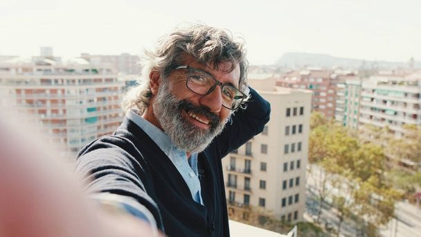 Close-up of mature man taking selfie while standing on balcony, looks at camera - Foto, Imagen