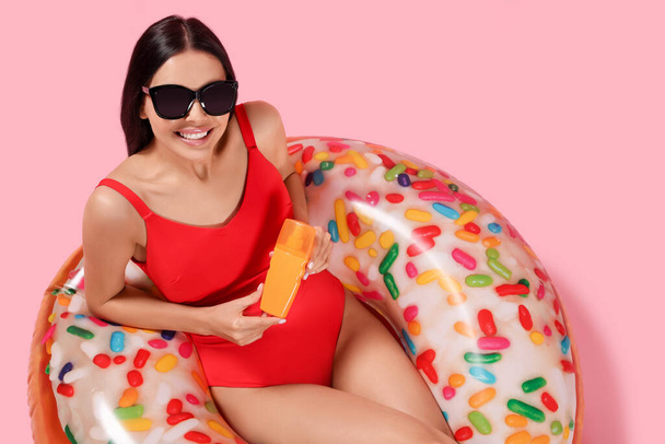 Young woman with sun protection cream on inflatable ring against pink background, above view - Foto, Imagen