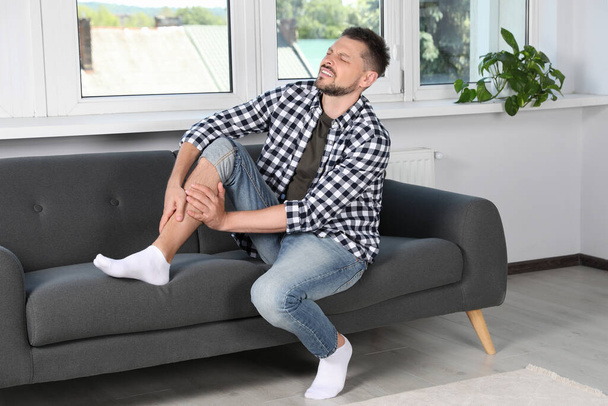 Man rubbing sore leg on sofa at home - Foto, immagini